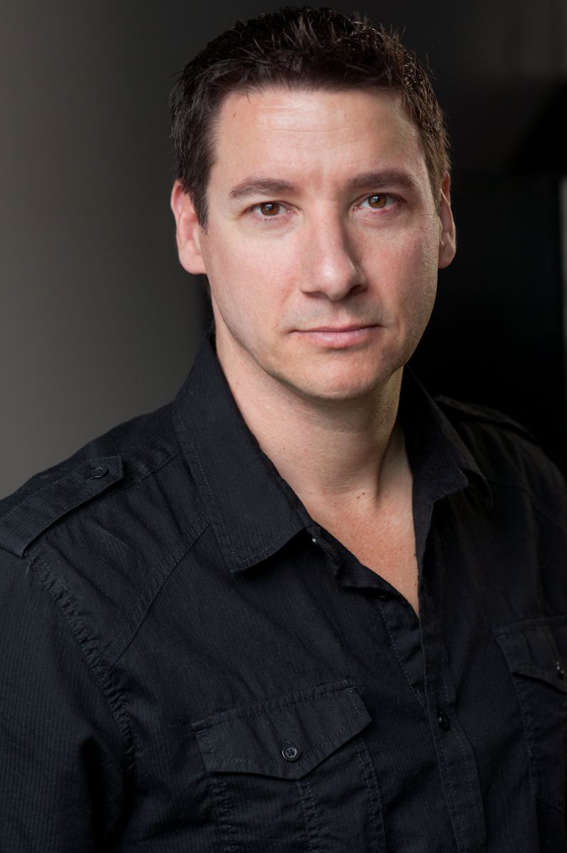A man with short, dark hair wears a black button-up shirt